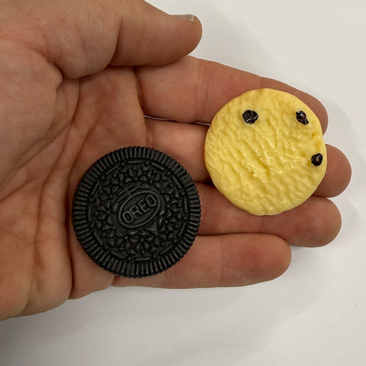 Hand holding a black Oreo cookie and a yellow cookie with chocolate chips against a white background